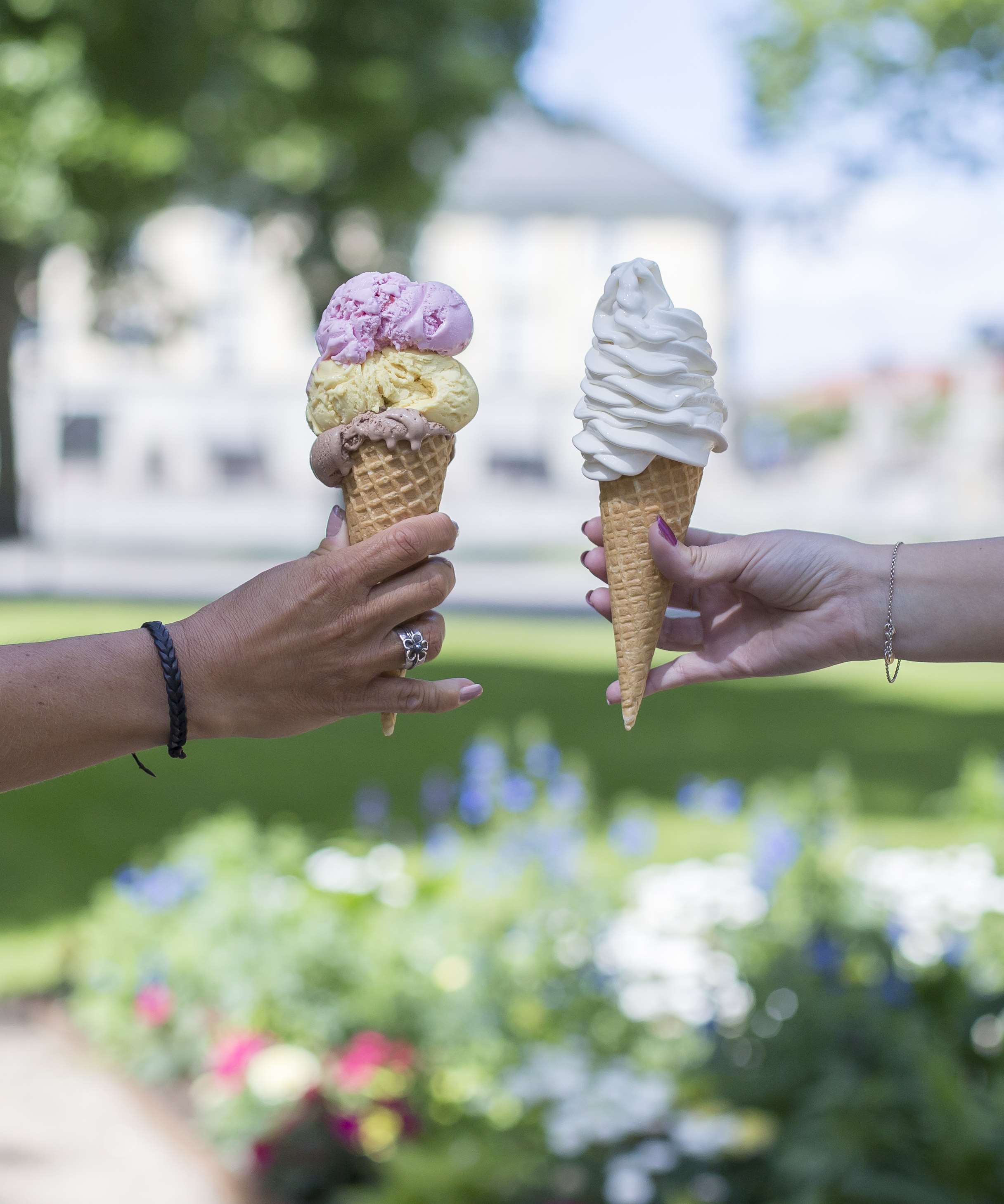 Två händer som håller i en mjukglass i strut och en kulglass i strut.