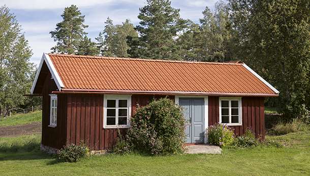 Rött torp med lertegelpannan Höganäs på taket i färgen naturröd. Blå dörr.