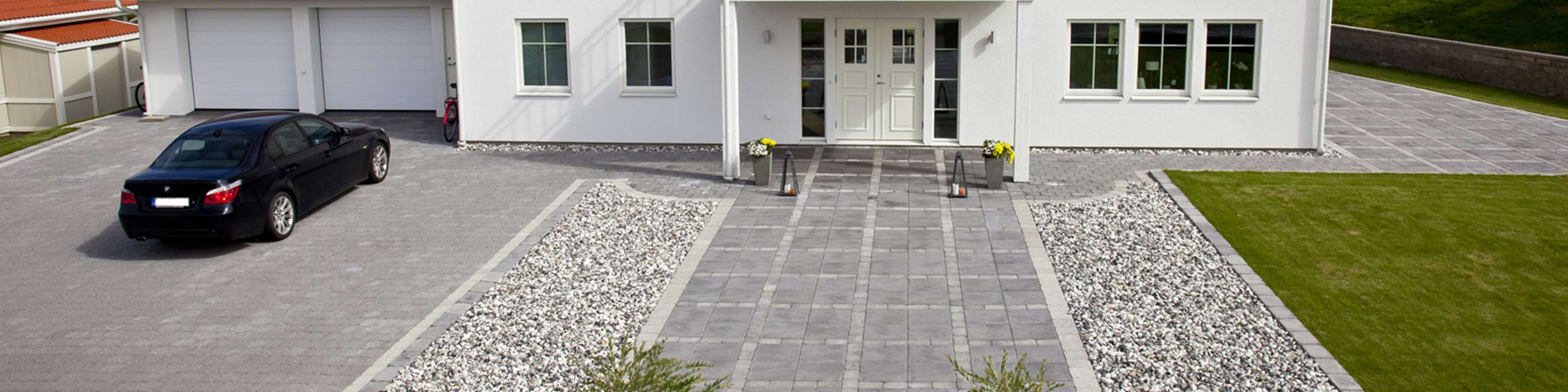 Vitt hus med markstensyta framför huset. En bil står parkerad på garageuppfarten.