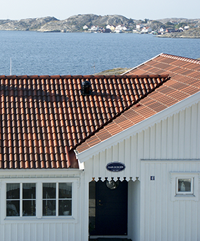Vitt hus med tegelrött tak framför vattnet.