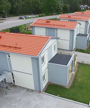 Vit/grått hus med tegelröda takpannor i en stadsmiljö.