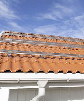 Tegelröda takpannor med solcellsinfästning på. Blå himmel som bakgrund.